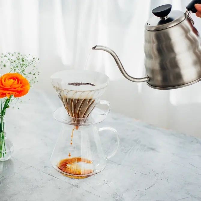 Håndbrygning af kaffe med stålkerkedel og filter over glaskande