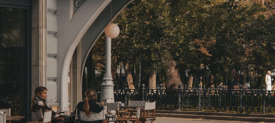 Caféterrasse med gæster under en overdækket bue ved efterårstræer