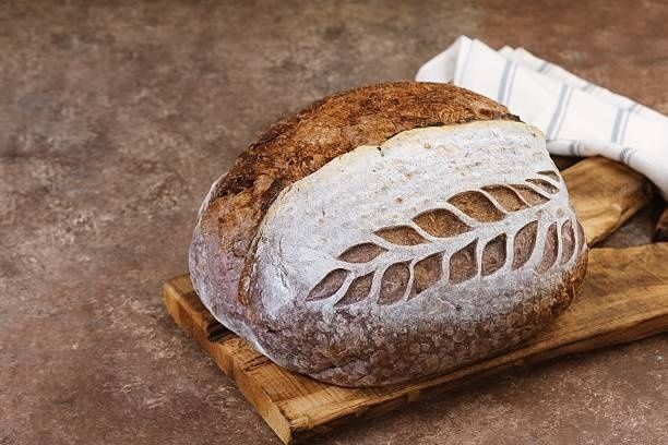 Rundt surdejsbrød med sprød, dekorativt snittet skorpe på et træbræt